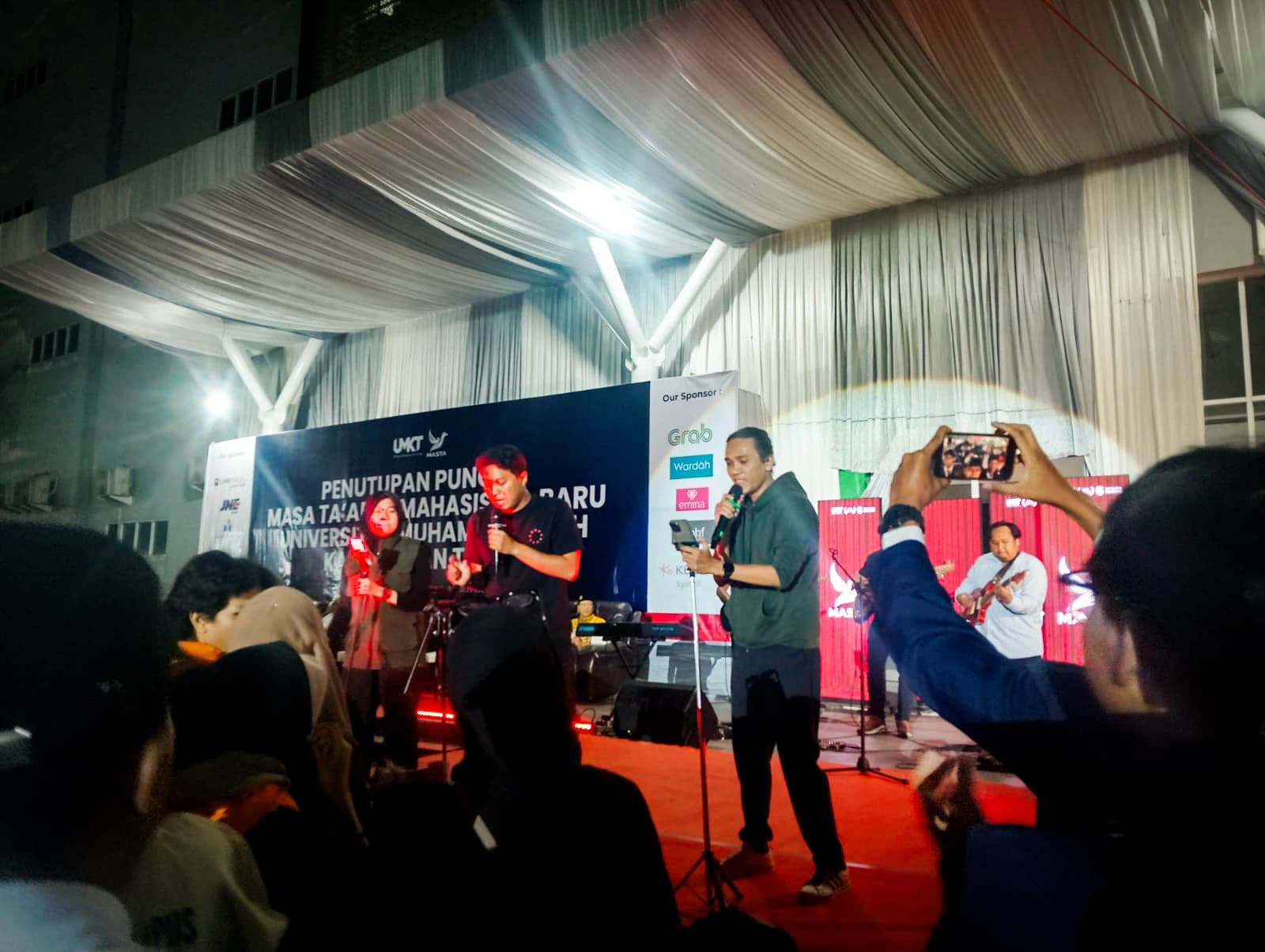 Penampilan band di panggung malam puncak: vokalis memegang mikrofon dengan gitaris dan pemain keyboard di belakangnya, berlatar spanduk penutupan MASTA