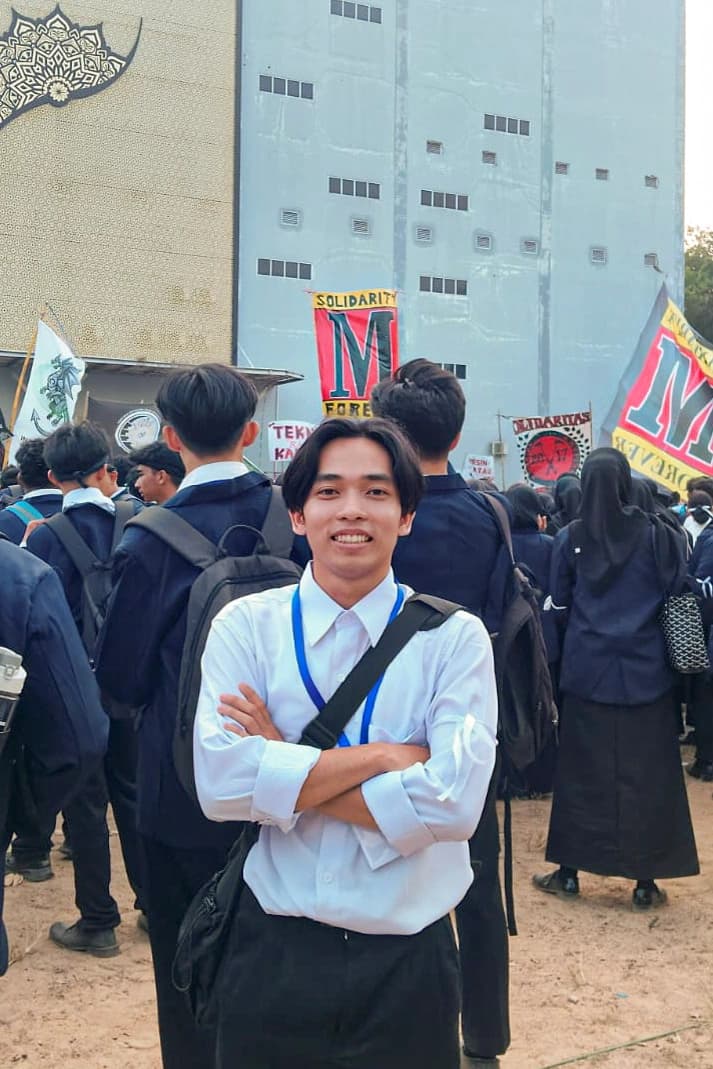 Potret penulis mengenakan kemeja putih dan tali pengenal, berdiri dengan tangan bersedekap di tengah kerumunan mahasiswa baru saat rangkaian MASTA berlangsung
