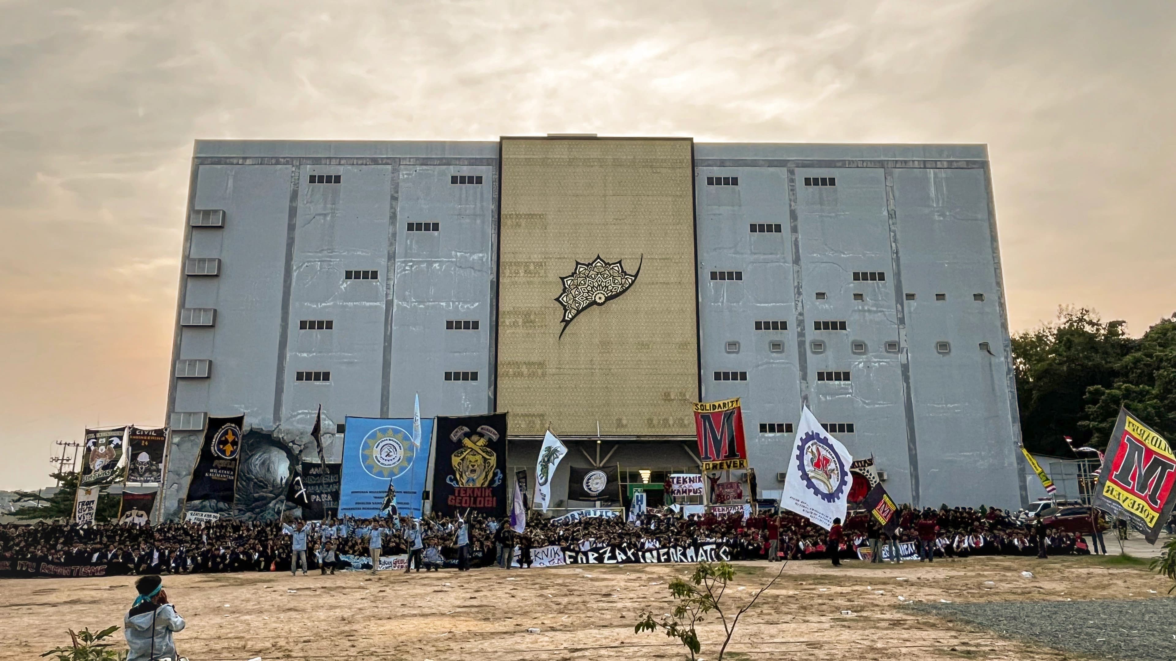 Gedung fakultas UMKT menjelang senja dengan ratusan mahasiswa baru berjas almamater berkumpul di depannya sambil membentangkan spanduk program studi teknik